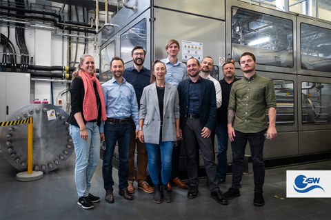 A group of people are standing together and smiling at the camera. They are in a mechanical environment.