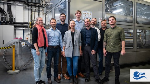 A group of people are standing together and smiling at the camera. They are in a mechanical environment.