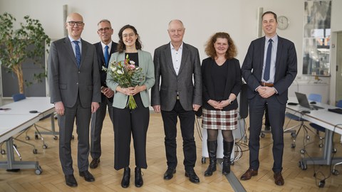 Menschen stehen in einer Reihe und schauen in die Kamera. Die Frau in der Mitte hält einen Blumenstrauß in der Hand.