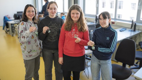 Eine Gruppe Mädchen stehen im Halbkreis und lächeln in die Kamera. In der Hand halten sie selbst hergestellte Flaschenöffner und Schlüsselanhänger.