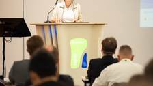 Eine Frau steht an einem Rednerpult und hält eine Rede.