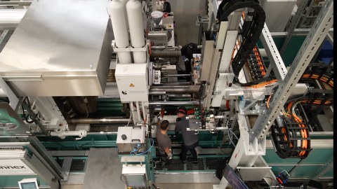 A machine is photographed from above. Two workers are standing at the machine and working.