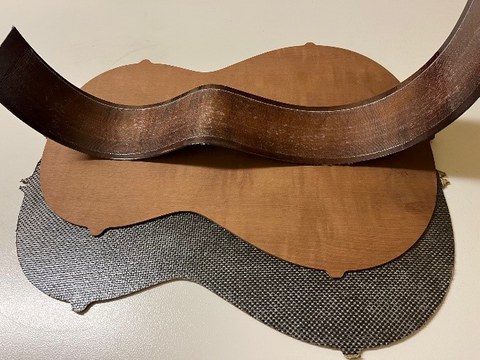 Im Bild sind die Gitarrenbauteile Boden und Zarge einer Konzertgitarre zu sehen. Diese sind mit einem textilen Faserhalbzeug verstärkt.