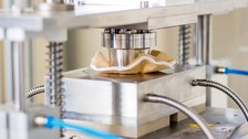 Fotos einer Pressvorrichtung aus Metall, die ein weiß und braunes Material einzieht.