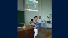 Foto einer Frau, die vor einem Publikum spricht. Im Hintergrund ist eine Präsentation "Wissen schafft Brücken" zu sehen.