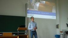 Vortragender Ludwig Schmidtchen mit Präsentation im Hintergrund.