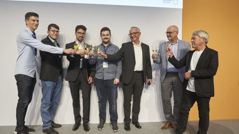 Photo of 8 men, raising their glasses with sparkling wine.