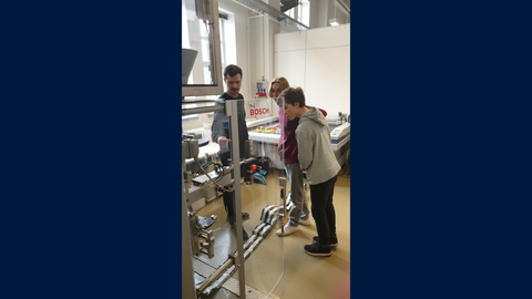 Drei Personen schauen eine Schlacuhbeutelmaschine an.