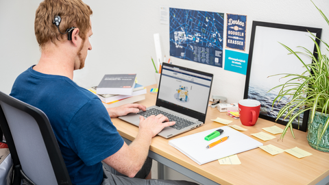 Photo of a student with hearing aid. He is sitting at a desk in front of his notebook.