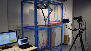 Delta robot with optical measuring system. In addition to delta kinematics with servo drives, a high-speed camera system with extra lighting can be seen. Computers for test rig control and measurement data recording can also be seen.