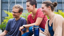 Foto: Drei Studenten sitzen beisammen. Eine davon hält einen TU Dresden Becher in der Hand.