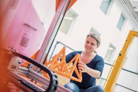 Auf dem Bild ist eine Frau zu sehen, die ein Brückenmodell aus Kunststoff in der Hand hält