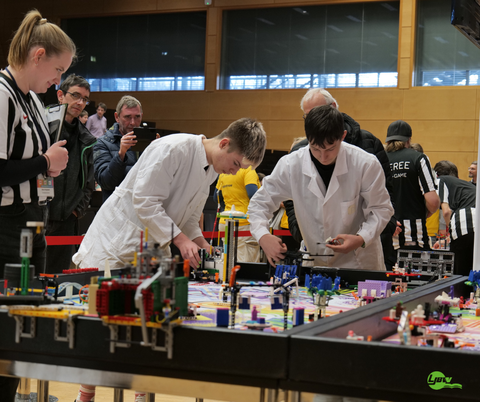 Zwei Schüler in weißen Kitteln an Robotik-Spielfeld