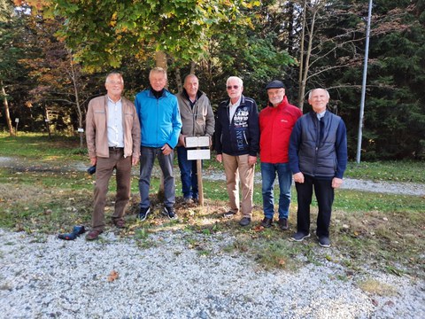5 elderly men under tree with sign for diploma anniversary