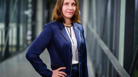 Junge Frau mit schulterlangen braunen Haaren in blauen Blazer posiert mit eingestützter Hand in der Hüfte