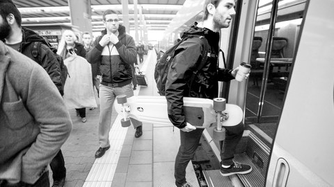 Ein junger Mann steigt in die U-Bahn ein und hält ein Skateboard unterm Arm.