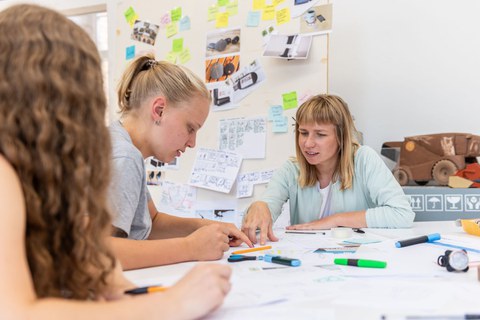 Auf dem Bild sind 3 Studentinnen zu sehen, die an einem Tisch sitzen