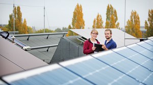 Foto der Photovoltaikanlage auf dem Dach des Zentrums für Energietechnik. Im Vordergrund sieht man Solarpanele, im Hintergrund zwei Personen.