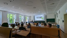 Personen sitzen im Hörsaal und schauen auf eine Projektion.