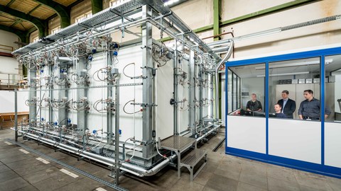Das Foto zeigt links eine begehbare Klimakammer. Rechts in einem extra Beobachtungsraum sieht man den SOMAK-Projektleiter Dr. Joachim Seifert (Mitte hinten) und sein Team.