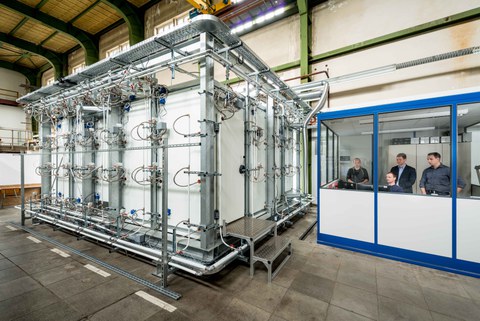 Das Foto zeigt links eine begehbare Klimakammer. Rechts in einem extra Beobachtungsraum sieht man den SOMAK-Projektleiter Dr. Joachim Seifert (Mitte hinten) und sein Team.