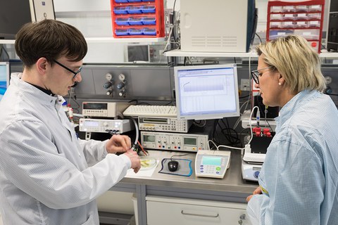 Das Foto zeigt Frau Staatsministerin Klepsch (rechts im Bild), die sich in den Laboren im Werner-Hartmann-Bau über das Projekt FlexEO informiert. Links im Bild sieht man einen jungen Mann, der der Staatsministerin etwas erklärt.