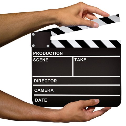 Auf dem Bild sieht man ein Filmklappe, die von sein Hände gehalten wird.