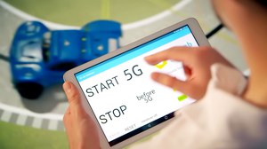 Auf dem Foto sieht man einen jungen Mann, der über ein Touchpad ein Miniaturauto auf einer Testrennstrecke mit 5G bedient.