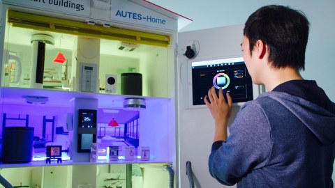 Auf dem Foto sieht man einen Mann, der über ein Touch-Panel ein Modell eines Smarthomes bedient.