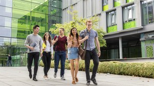 Foto von Studierenden, die vor dem Andreas-Pfitzmann-Bau auf den Betrachter zu laufen und sich dabei unterhalten. 
