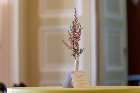 Das ausgedruckte Programm des Summer Get-Togethers steht an eine Blumenvase gelehnt auf einem Stehtisch.
