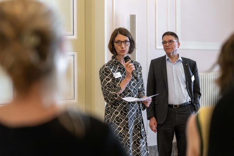Professorin Roswitha Böhm, Prorektorin Universitätskultur, spricht in ein Mikrofon. Professor Ronald Tetzlaff ist im Hintergrund zu sehen.