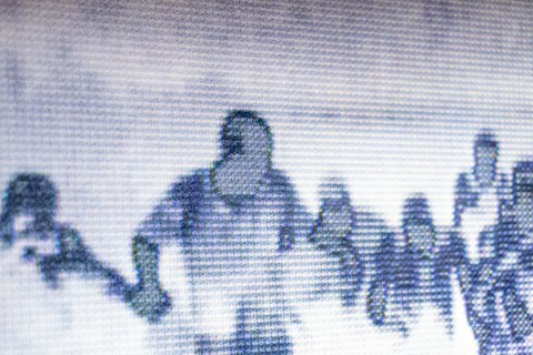 Von nahem fotografierter Bildschirm. Auf dem Bildschirm ist ein schemenhaftes Bild von flüchtenden Menschen zu sehen.
