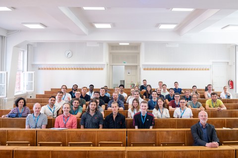 Gruppenbild der Teilnehmenden in einem Hörsaal auf Holzbänken sitzend.