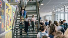 Das Foto zeigt eine Treppe im Foyer des Hörsaalzentrums der TU Dresden. Im Foyer befinden sich viele Menschen. Auf den Treppenstufen gehen einige Personen nach oben.