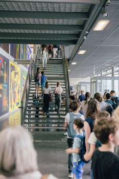 Das Foto zeigt eine Treppe im Foyer des Hörsaalzentrums der TU Dresden. Im Foyer befinden sich viele Menschen. Auf den Treppenstufen gehen einige Personen nach oben.