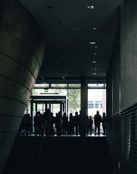 Das Foto zeigt eine Menschentraube, die sich in einem Foyer befindet. Die Farbgebung des Fotos ist sehr dunkel, es sind nur Silhouetten zu erkennen.
