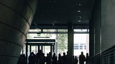 Das Foto zeigt eine Menschentraube, die sich in einem Foyer befindet. Die Farbgebung des Fotos ist sehr dunkel, es sind nur Silhouetten zu erkennen.