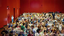 frontaler Blick in einen Vortragssaal, viele Kinder sitzen auf Stühlen