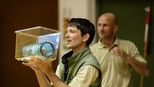 Ein Mann hält einen durchsichtigen Behälter in seinen Händen, in dem eine Rolle aus Kunststoff liegt.