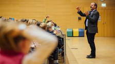 Ein Mann steht vor einem Publikum aus Kindern und erklärt etwas.
