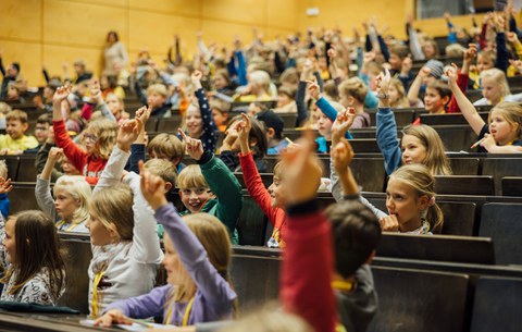 Viele Kinder heben die Hände und stellen Fragen.