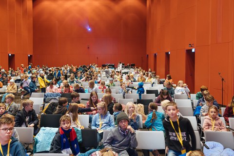 Ein Blick in den Saal. Viele Kinder sitzen schon in den Sitzreihen.