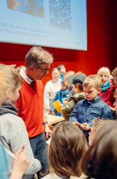 Der Dozent unterhält sich mit Kinder, die um ihn herumstehen.
