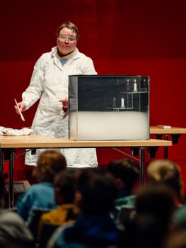 Eine Forscherin steht an einem Tisch. Auf dem Tisch steht ein Experiment mit Kerzen.