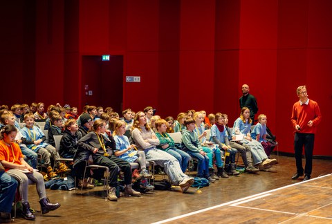 Viele Kinder sitzen in einem Saal.