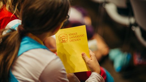 Ein Mädchen hält das Schreibheft der Kinder-Uni in der Hand.