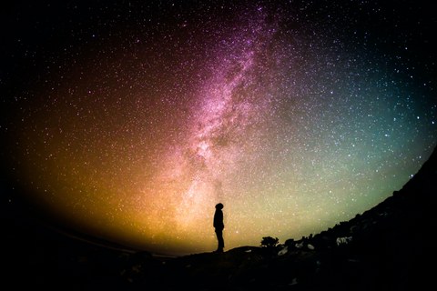 Das Bild zeigt den Nachthimmel mit vielen Sternen. Am unteren Bildrand ist die Silhoutte eines Menschen zu erkennen, der in den Himmel schaut.