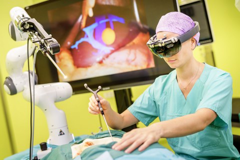 Das Foto zeigt eine Chirurgin im Operationssaal. Sie trägt eine VR-Brille und hantiert mit einem Endoskop.
