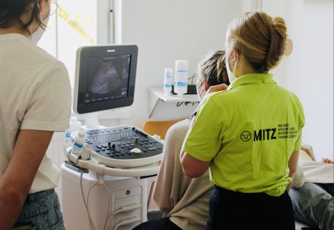 Tutorin mit grünen T-Shirt erklärt Lernende Person etwas am Sonographiegerät